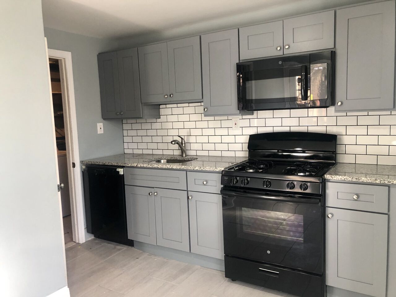 Kitchen with gray shaker cabinets, granite, and white subway tile