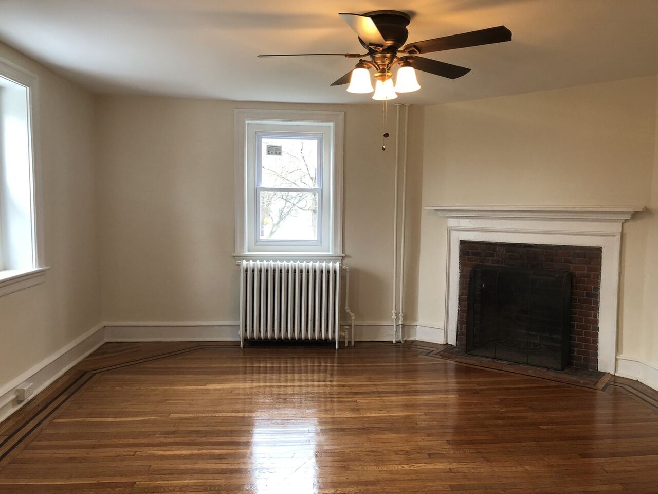 Living room with brick fireplace, white mantel, and inlaid hardwood floors